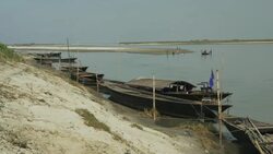 A steeply eroded river bank in Northern Bangladesh is shown with wooded boats moored on the sand Stock Footage