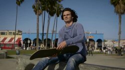 teenager sitting on rail playing with his skateboard looking ahead venice California skatepark Stock Footage