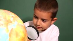 Boy looking through magnifying glass at globe Stock Footage