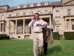 Wide shot man talking on cell phone in front of mansion / butler rushing up and putting blazer on man Stock Footage