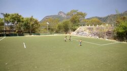 Young Brazilian boys play soccer match on turf field with Christ the Redeemer in distance Stock Footage