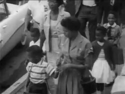 B/W 1950s high angle PAN Black parents walking their children to desegregated school / newsreel Stock Footage