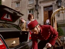 Low angle medium shot bellman loading luggage into trunk of limo as woman looks on / man talking on cell phone Stock Footage