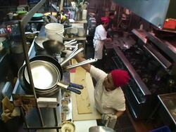 A dishwasher stacks pans as a chef cooks at a stove in a kitchen. Stock Footage