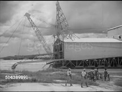 1953: MINING INDUSTRY: TIN: WS Armored car down dirt road, armed Engineers Roderick Caldwell & Steven Littledyke walking toward dredge. VS Bucket-line dredge working, water flowing out of stern chutes, buckets scooping & pulling, mud dumping. Instructional Video