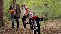 Children in skeleton costumes running in woods with parents Stock Footage