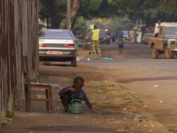 MS Shot of small boy brushing his teeth on side of road and people walking around / Conakry, Guinea Stock Footage