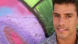 Young Brazilian man leaning on graffitied wall turns and smiles at camera Stock Footage