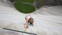 Female rock climber ascends artificial holds on concrete dam Stock Footage