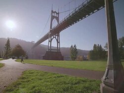 WS DS SLO MO Shot of young boy energetically running down sidewalk path in front of St. Johns Bridge along waterfront / Portland, Oregon, United States Stock Footage