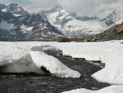 Creek flows from snowpack towards distant mountains Stock Footage