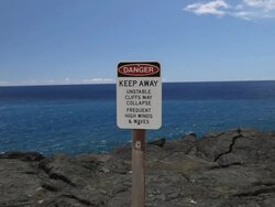 MS PAN Shot of danger sign on volcanic cliff edge in Volcanoes National Park with ocean / Volcano, Hawaii, Big Island, United States Stock Footage
