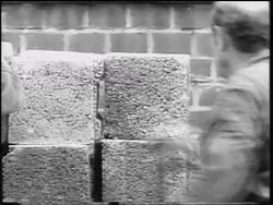 B/W 1961 REAR VIEW construction worker grabs concrete block from pile / construction of Berlin Wall Stock Footage