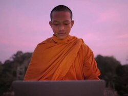 CU A Buddhist monk types on a laptop computer on top of an ancient temple at sunrise in Angkor Wat / Siem Reap, Cambodia Stock Footage