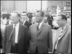B/W 1961 three men in suits standing on West Berlin street during construction of Berlin Wall Stock Footage