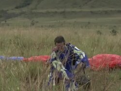 A paraglider claps and kisses the ground with a parachute strapped to his back. Stock Footage