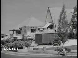 1940: DUTCH EAST INDIES: Churches, large houses in residential neighborhoods. Dutch family of four eating meal in dining room w/ Indonesian male in chef's coat serving coffee. Framed photo of Queen Wilhelmina Queen Wilhelmina of Netherlands on wall. Instructional Video
