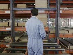 WS TS worker riding retrieval lift in multi-story warehouse for pre-cut wood in furniture factory, rear view Stock Footage
