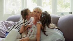 Granddaughter s kissing Grandmother 's cheeks on sofa Stock Footage