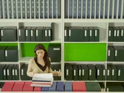 HA WS office library, woman enters frame from left, picking up documents and exits frame left Stock Footage