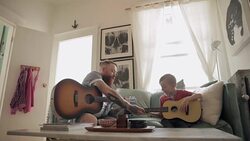Father teaching son playing guitar on living room sofa Stock Footage