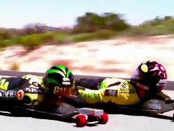 OVEREXPOSED wide shot tracking shot zoom in to close up two street lugers speeding on mountain road Stock Footage