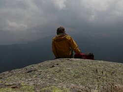 PAN to hiker descending to alpine pond, scoops water Stock Footage