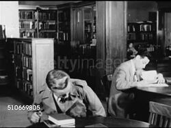 1949: DRAMATIZATION: Young teenage male sitting at library table w/ book, checking spine, opening.   Public library. Instructional Video