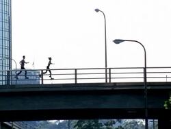 Wide shot woman and two men running across bridge on skyrunners Stock Footage