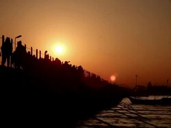 Early morning sun rises in sky as silhouetted devotees slowly cross pontoon bridge, metallic looking river streams below them.  Kumbh Mela, India Stock Footage