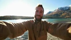 Cheerful man in nature takes selfie portrait near lake Stock Footage