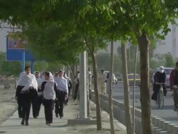Headcovered schoolgirls, bicycle and motor traffic advance up the street Stock Footage