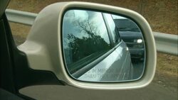 A white side-view mirror reflects the headlights of a truck behind the car. Stock Footage