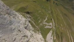 POV wingsuit flying down a cliff face and over alpine meadow Stock Footage