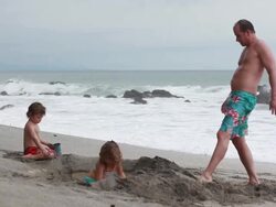 MS PAN Man standing and kicking sand as kids play in sand on beach / Montezuma, Puntarenas, Costa Rica Stock Footage