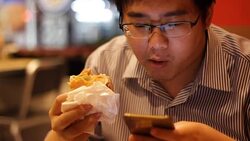 man using smartphone while eating hamburger Stock Footage