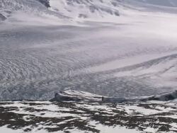 Wide Shot aerial - A vast, snowy landscape dwarfs an adult standing on a cliff's edge near the mountains / Alaska, USA Stock Footage