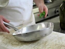 Close up shot of a chef putting fresh basil into a oiled pan Stock Footage