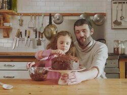 MS Shot of Daddy and daughter sitting at kitchen table adding chocolate icing to cake / London, United Kingdom  Stock Footage
