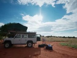 MS T/L Shot of People busy packing up camp equipment to stow in all terrain vehicle under streaming cloudscape, over blue sky / Kalahari, Windhoek, Namibia Stock Footage