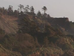 Medium Long Shot pan-right - Seagulls fly over an eroded coastal hill as waves break against rock formations close to shore/Oregon Stock Footage