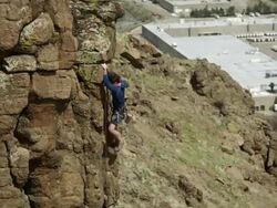 Man climbs a steep rock face with buildings below. Stock Footage