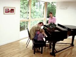 High angle wide shot man giving son and daughter piano lesson as wife looks on / pan to picture on wall Stock Footage