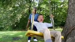 MS Laughing young boy leaning back looking at father while swinging on backyard swing Stock Footage
