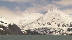 The Arctic Ocean flows near ice-covered mountains in Alaska on a partly cloudy day. Stock Footage