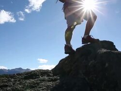 Hiker ascends to prow of rock protruding over valley, mtns & lake below Stock Footage