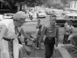 B/W 1950s senior woman guiding children past camera into school / pro-segregation protests / news. Stock Footage