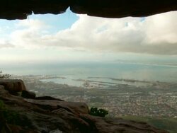 WS PAN View of man walking through edge of cave opening and waterfall falling over opening wit Cape Town landscape / Cape Town, Western Cape, South Africa Stock Footage