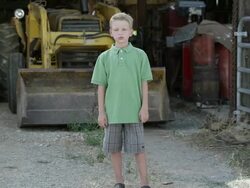 Slow motion push of boy with cleft lip standing in front of tractor. Stock Footage
