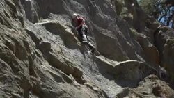 A young man rock climbing on a mountain with a woman belaying him. Stock Footage